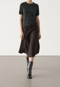 Tummanharmaa lyhythihainen neule yhdistettynä ruskeaan A-linjaisiin hameeseen. Polven ylle ulottuvat mustat nahkasaappaat täydentävät asua. Pintakuvio tasainen.