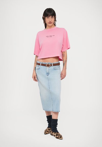 Ροζ κοντομάνικη μπλούζα με το κείμενο "Καλές στιγμές και σημάδια από τον ήλιο", συνδυασμένη με φούστα από ανοιχτό μπλε τζιν, καφέ ζώνη και παπούτσια με ζωικό σχέδιο.