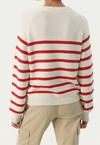 Biały sweter z dzianiny z wyraźnymi czerwonymi poziomymi paskami, ściągaczami przy mankietach i u dołu, oraz rękawami raglanowymi. Teksturowany materiał o luźnym kroju.