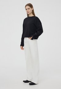 Czarna bluza z kokardkami na rękawach, zestawiona z białymi szerokimi spodniami i czarnymi butami. Prosty design, miękka tkanina, casualowy krój.