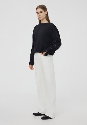 Felpa nera con fiocchi sulle maniche, abbinata a pantaloni bianchi a gamba larga e scarpe nere. Design semplice, tessuto morbido, vestibilità casual.