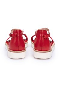 Sandali in pelle rossa con una finitura liscia, dotati di una tracolla regolabile e suole in gomma bianca per un tocco di contrasto. Design aperto sul retro con dettagli minimi.