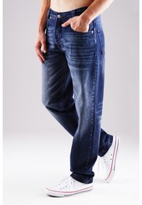 Dunkelblaue Jeans aus Denim mit geradem Schnitt, ausgestattet mit fünf Taschen und dezentem Verblassen. Getragen mit weißen Sneakers mit roten Akzenten.