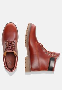 Bruna läderstövlar med en slät yta, rundad tå, snörning framtill, kontrasterande svart klack och en robust gummisula.