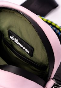 Binnenkant van een tas met roze leren details, groene stofvoering, een zwart label met "Chloé Goldrenner," en een ritsvak.