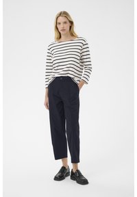 Haut léger à rayures, à manches longues, en blanc et marine, associé à un pantalon large marine et des chaussures noires à semelle épaisse.