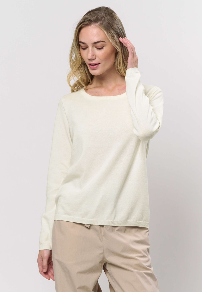 Crèmewitte trui met lange mouwen en ronde hals, gemaakt van zachte stof. Beschikt over een losse pasvorm en een effen textuur, gecombineerd met beige broek.