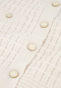 Witte gebreide cardigan met een textuurpatroon, ronde knopen met reliëflogo en ribbelaccenten langs de randen.