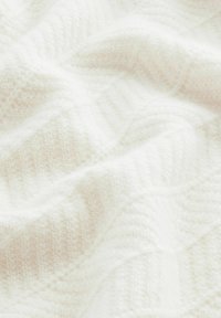Tissu tricoté blanc avec un motif texturé et ondulé. Apparence douce et pelucheuse, présentant une couleur claire et neutre avec de subtiles variations.