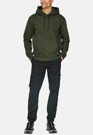 Olijfgroene hoodie met een voorzak, gecombineerd met zwarte cargobroek met ritsen. Gemaakt met meerkleurige sneakers.