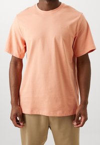 Camiseta de manga corta en tejido de algodón melocotón, con escote redondo, que presenta un pequeño logotipo de Nike bordado en el pecho. Diseño simple y limpio.