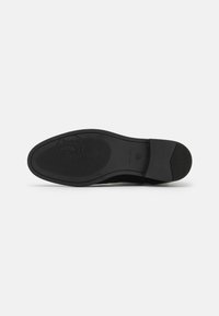 Suola di una scarpa, in gomma nera piatta, superficie testurizzata, con un logo circolare e un motivo scanalato per una migliore presa, senza dettagli di design visibili.