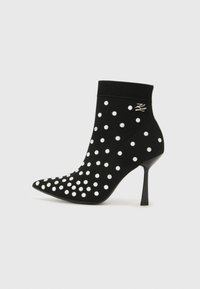 Black ankle boot with a pointed toe, made of soft material, featuring white polka dots and a high stiletto heel. Knitted cuff at the top.