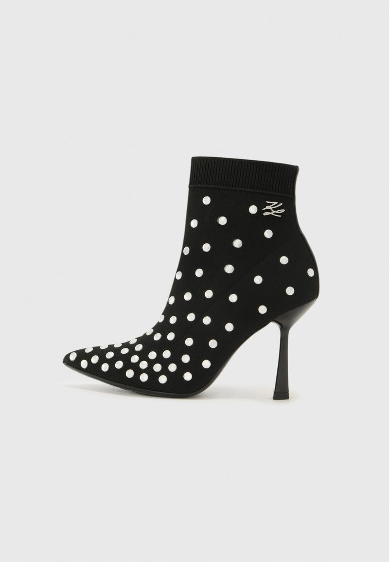 Black ankle boot with a pointed toe, made of soft material, featuring white polka dots and a high stiletto heel. Knitted cuff at the top.