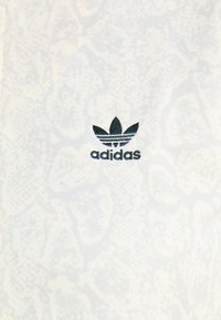 Bílá tkanina s jemným texturovaným vzorem. Obsahuje černé logo Adidas se třemi lístkovými akcenty a třemi vodorovnými pruhy pod nimi.