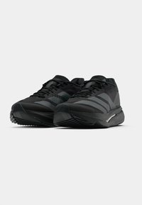 Chaussures de sport noires avec empeigne en mesh, rayures ton sur ton, col rembourré et semelle texturée. Présentent un design élégant et profilé pour la performance.