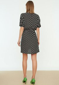 Kurzes schwarzes Kleid mit weißen Punkten, tailliert, kurzen Puffärmeln und weitem Rock. Kombiniert mit grünen High Heels.