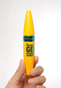 Żółta tubka tuszu do rzęs z zwężającą się pokrywką, z turkusowym paskiem oznaczonym "Maybelline" oraz "the COLOSSAL GO EXTREME WATERPROOF" napisanym pogrubioną czcionką.