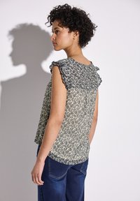 Hihaton paita vaaleassa kermassa, jossa on tummansinisiä lehtikuvioita. Paidan olkaimia somistavat röyhelöt, ja se on hieman A-linjainen. Pehmeää kangasta, jossa on kevyt rakenne.