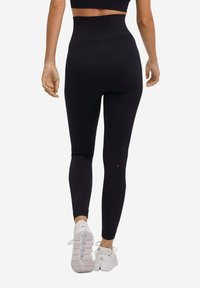 Zwart high-waisted leggings met een gestructureerde afwerking. Voorzien van rode letters op de enkels die "L" en "R" aangeven. Gepaard met witte sportschoenen.