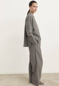 Set di abbigliamento da loungewear a righe grigie e bianche composto da una camicia a maniche lunghe con bottoni e pantaloni a gamba larga. Superficie texturizzata, design rilassato.