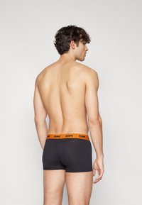 Sorte boxershorts med en oransje DIM-logo på midjebåndet, med en tettsittende design og glatt bomullsstoff, sett fra bak.