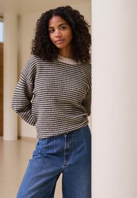 Pull en tricot à rayures horizontales beige et marine, col rond, associé à un jean en denim bleu taille haute. Tissu texturé.