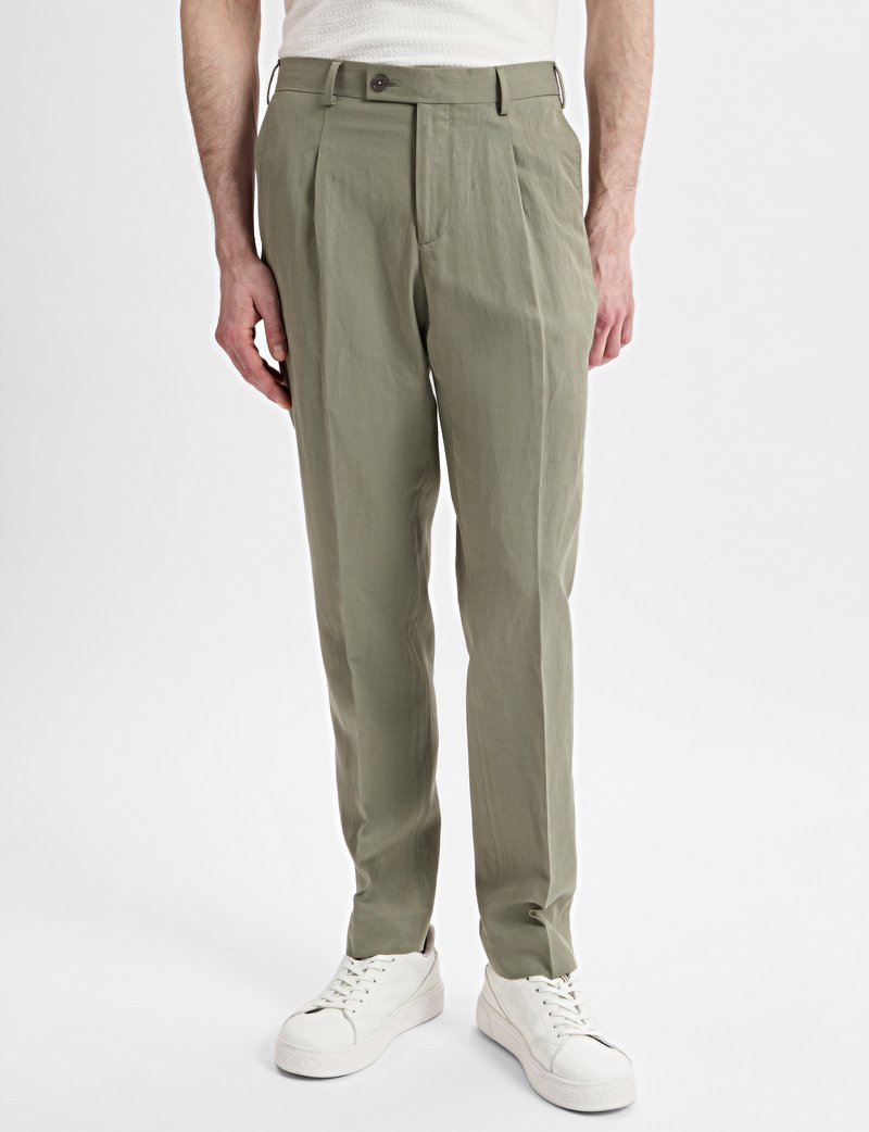 Trousers in light olive green fabric, featuring a straight cut, pleats, and a button closure. Paired with white sneakers.