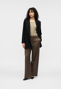 Μαύρο σακάκι πάνω από μια μπεζ μπλούζα, σε συνδυασμό με καφέ παντελόνια φαρδιάς γραμμής. Φορεμένο με μαύρες μυτερές γόβες. Λείο ύφασμα και άνετη εφαρμογή.