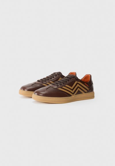 Sneakers din piele maro cu accente portocalii și suprapunerile texturate, având un model zigzag distinctiv și o talpă din cauciuc de tip gumă.