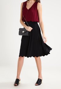 Burgundy sleeveless top with textured pattern, paired with a black flared skirt featuring a scalloped hem, and black open-toe mules.
