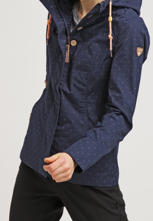 Mörkblå jacka med prickar som har en luva, ljusorange snörning och subtila sömnadsdetaljer. Tillverkad av slitstarkt tyg med fickor.