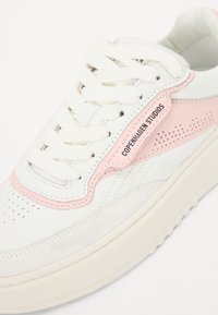 Hvit sneaker med rosa semsket detaljer, perforerte detaljer og hvite snører. Har merkeetikett "COPENHAGEN STUDIOS" på siden.