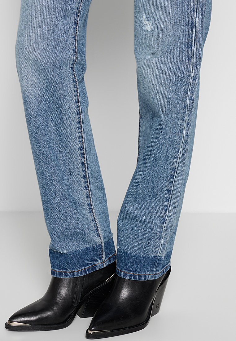 Jeans in denim blu con leggera usura indossati con stivaletti neri a punta con tacco a blocco e punte metalliche.