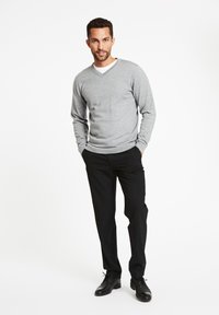 Pullover grigio a scollo a V realizzato in materiale morbido, abbinato a pantaloni neri. L'outfit presenta una vestibilità classica ed è completato da scarpe nere.