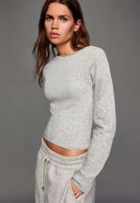 Jasnoszary sweter z długim rękawem o prążkowanej strukturze i okrągłym dekoltem, zestawiony z szarymi spodniami dresowymi. Prosty, casualowy design w neutralnych kolorach.