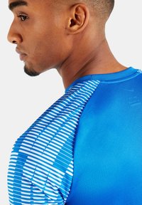 Blaues Sportshirt aus strukturiertem Stoff, mit kurzen Ärmeln und einem Streifenmuster auf der Schulter mit kontrastierenden weißen Linien.