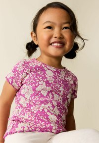 Rövid ujjú, rózsaszín virágos felső texturált bordázott mintával és hullámos szegéllyel. Élénk háttéren fehér virágmintákkal díszítve.