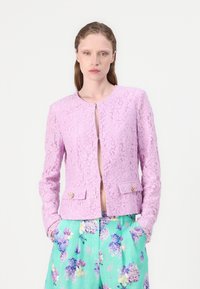 Lilla blonderjakke med intrikate blomster mønstre, frontlukking og gullfargede knapper; kombinert med mintgrønne bukser med blomstertrykk.
