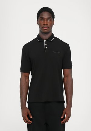 Svart polo skjorte med hvite krageakcenter og knapper, med en logo på venstre bryst. Glatt stoff, korte ermer, avslappet passform.