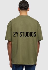 Alyvmedžio spalvos marškinėliai su laisvu siluetu ir apvalia kaklo iškirpte. Didelis juodas užrašas "2Y STUDIOS" atspausdintas ant nugaros su subtiliu rašysenos detaliu žemiau.