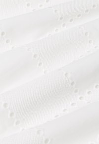 Hvidt stof med en tekstureret overflade og små, jævnt fordelte udskårne huller. Materialet har et blødt, glat udseende.