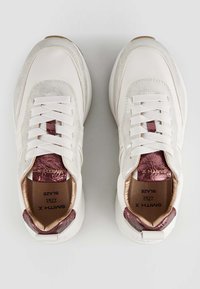 Sneakers bianchi con un accento bordeaux lucido e testurizzato sul tallone. Presentano lacci bianchi, soletta ammortizzata e finitura liscia.