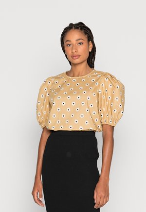 Blusa de manga curta, mostarda, com padrão floral branco, mangas bufantes e decote redondo, combinada com uma saia preta com relevo.