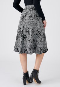 Zwart-witte rok met een bloemenpatroon en een uitlopende ontwerp, gemaakt van gestructureerde stof. Draagt zwarte enkellaarsjes met ritsen.