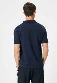Mörkblå polo med strukturerad stickning, kort ärm och klassisk krage. Har korta sidsprund i nederkanten för ökad komfort.