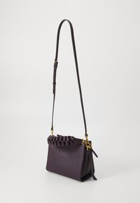 Borsa a tracolla in pelle viola con manico intrecciato, dettagli in metallo dorato e una lunga tracolla regolabile. Texture liscia e forma strutturata.