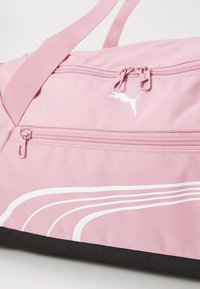Sac de sport rose avec accents et logo blancs, featuring deux compartiments zippés et un tissu texturé. Base inférieure noire.