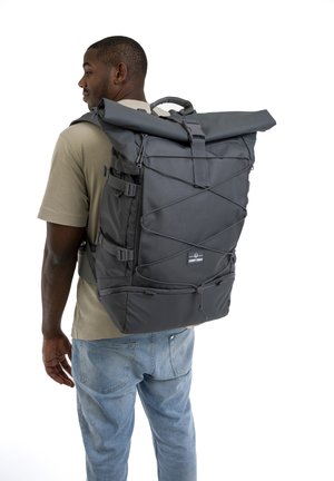 Black roll-top backpack with adjustable straps, made of durable fabric. Features elastic cord detailing and a logo patch on the front.