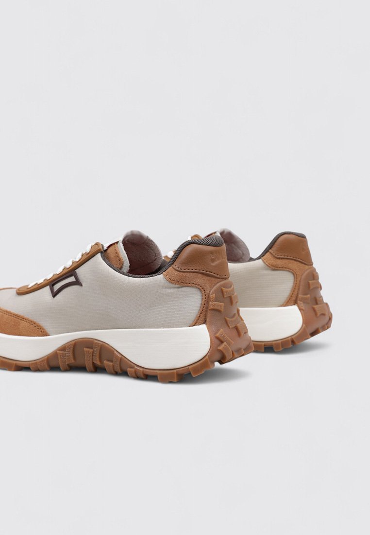 Beige canvas sneakers met bruine leren accenten, gestructureerde rubberen zool, ronde vorm en witte tussenzool; inclusief logodetail aan de zijkant.